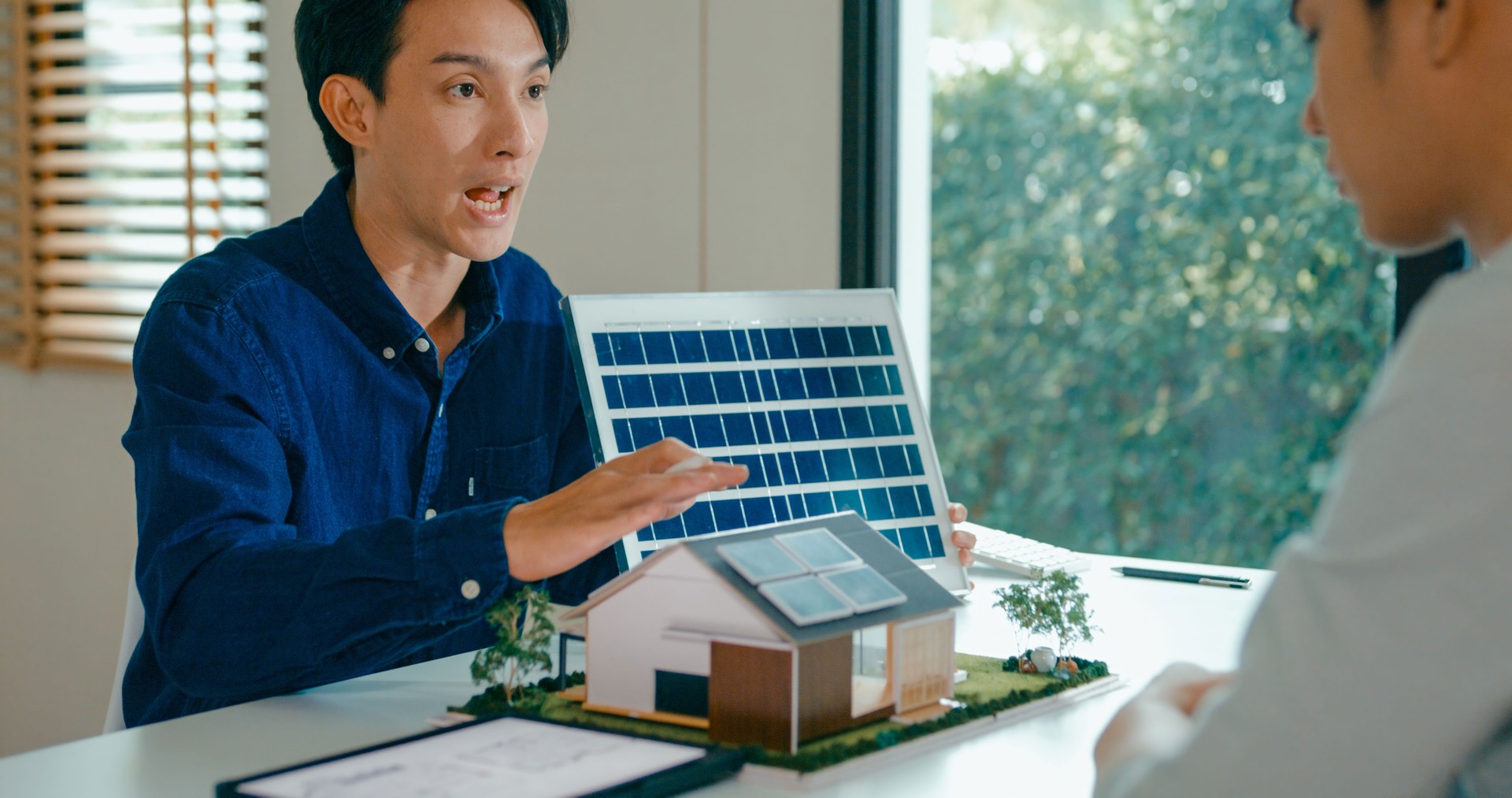 Young Asian couple in detailed consultation with real estate agent, who is highlighting advantages of home with solar panels. Consulting on Eco-Friendly Home Ownership with Real Estate Agent.